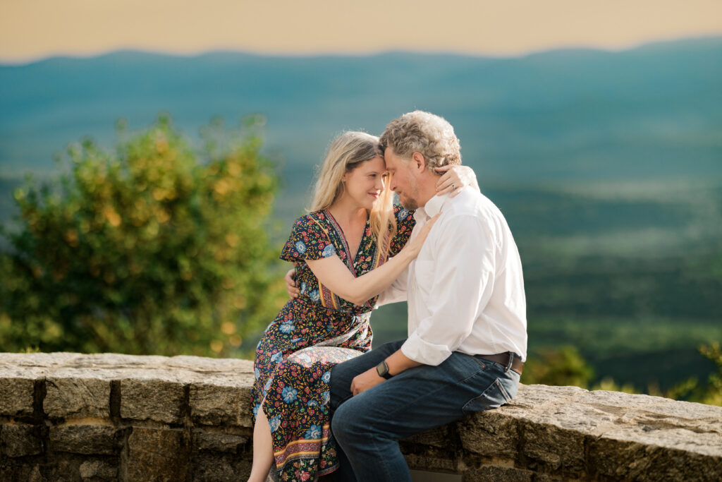 Couple sitting on a scenic stone wall during Amicalola Falls engagement photos with mountain sunset views