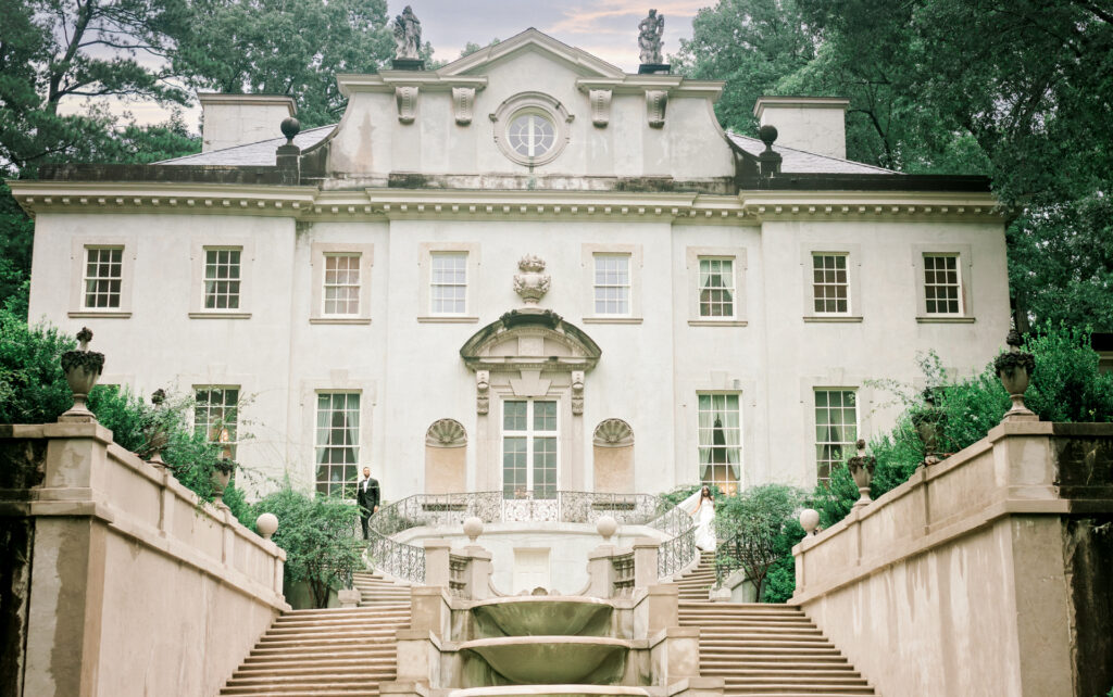 Iconic wide shot of Swan House Atlanta History Center during a rainy luxury Atlanta wedding day bride and groom walking down staircase on either side. 
