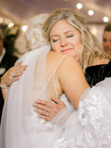 Emotional wedding photo of a bride holding back tears during a meaningful reception hug with mom.