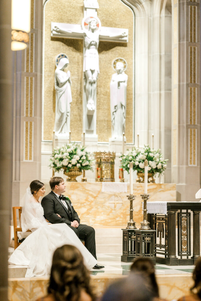 Bride and groom seated during Catholic wedding ceremony at Christ the King Cathedral in Atlanta Georgia