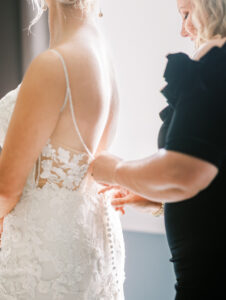 Bride standing beside a window showing the detailed back of her wedding gown during private Lake Mary wedding preparations