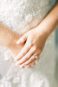 Close-up editorial photograph of a bride’s wedding ring and lace gown during bridal preparations