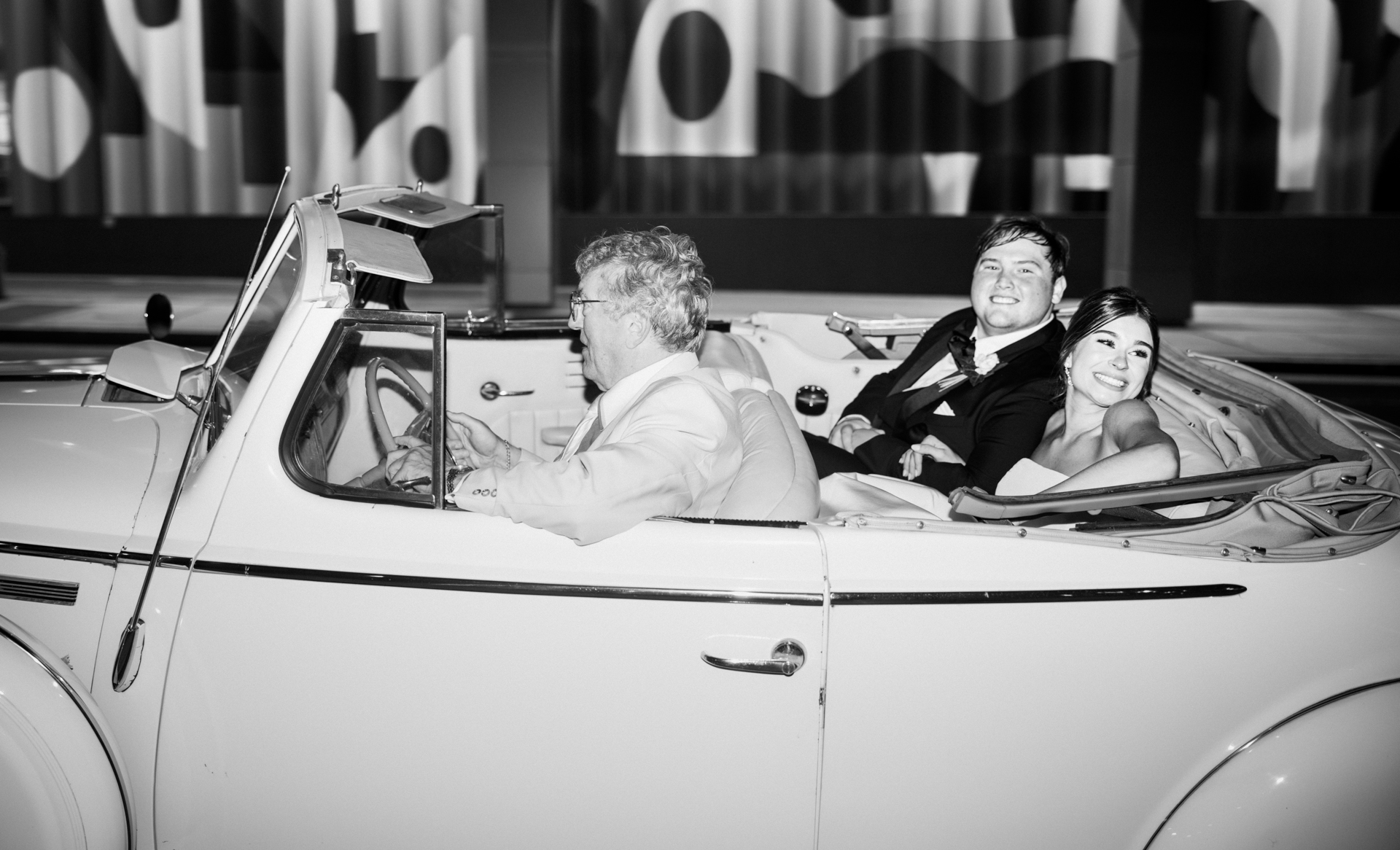 Black and white portrait of bride and groom riding in classic getaway car after Atlanta wedding