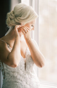 Bride adjusting her earrings beside a softly lit window during bridal preparations at a private Lake Mary wedding