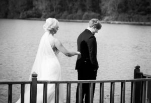 Emotional wedding photo of a bride approaching her groom during a lakeside first look captured by a Luxury Atlanta Wedding Photographer