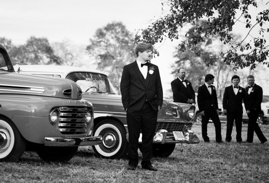 Black and white portrait of groom standing beside vintage trucks with groomsmen during a private Lake Mary wedding