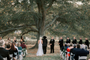 Wide view of outdoor private estate wedding ceremony beneath large oak trees at Lake Mary