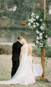 Bride lays head on grooms shoulder beneath floral cross during an outdoor private estate wedding
