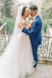 Timeless Swan House wedding portrait of bride and groom sharing a balcony kiss above the scenic grounds and fountains captured by a luxury documentary Atlanta wedding photographer