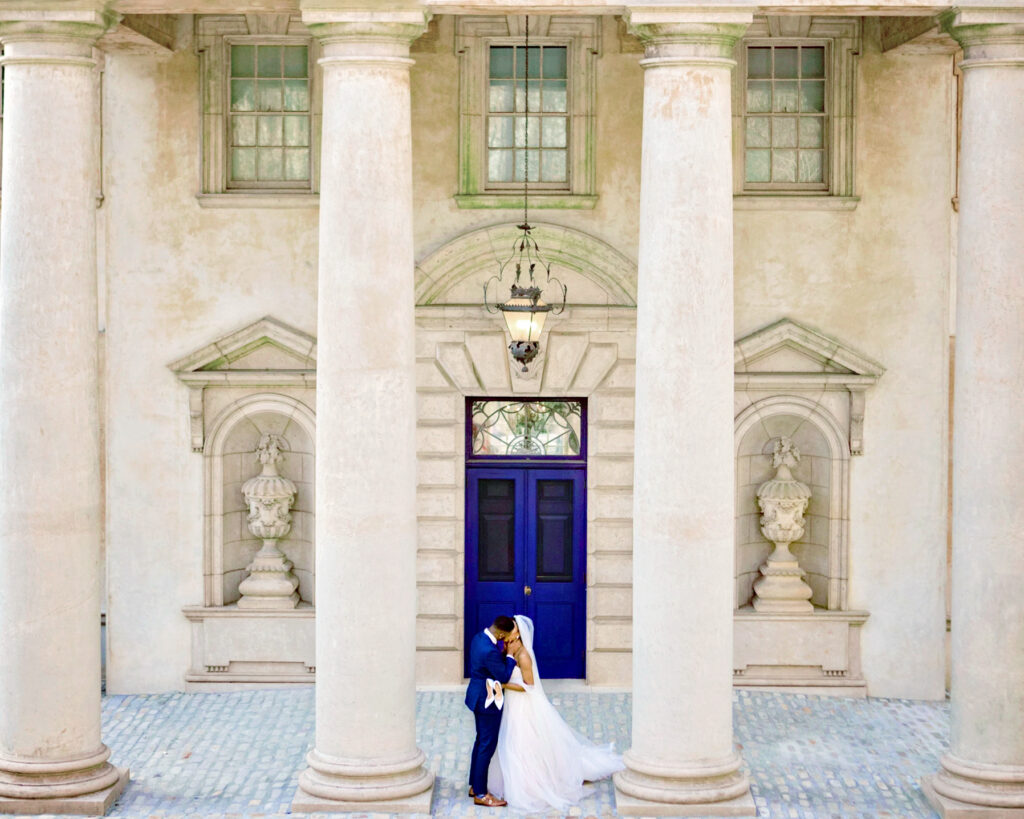 Luxury documentary Atlanta wedding photographer capturing bride and groom beneath grand columns and iconic blue doors at Swan House in Atlanta