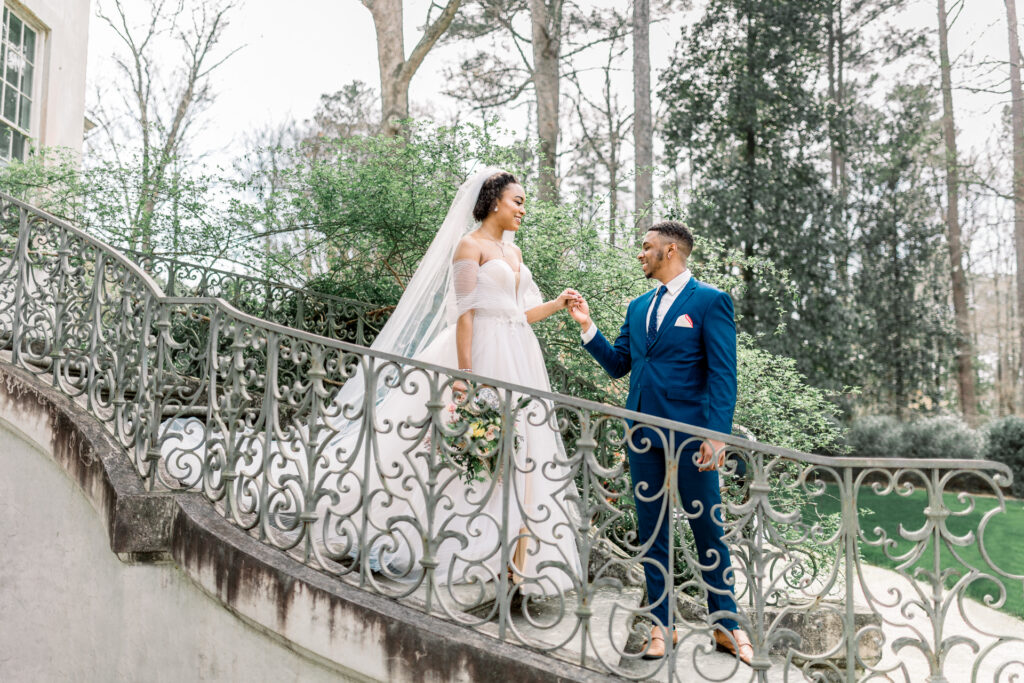 Bride and groom smiling at each other on the grand curved staircase at Swan House captured by a luxury documentary Atlanta wedding photographer